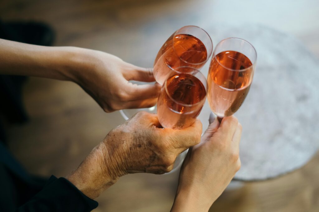 Three hands holding and clinking rose champagne glasses in a celebratory toast.
